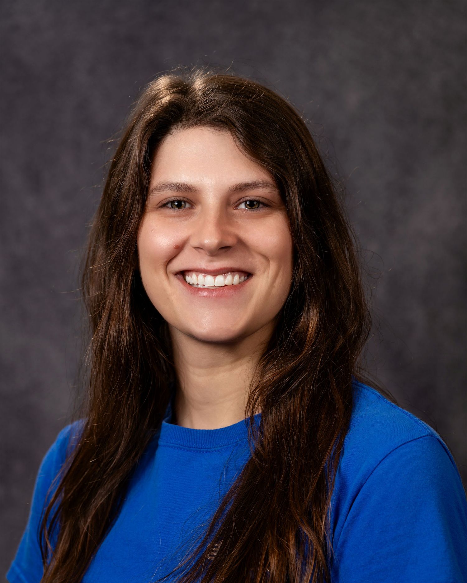 Professional headshot of someone in a bright blue top against a dark gray background.
