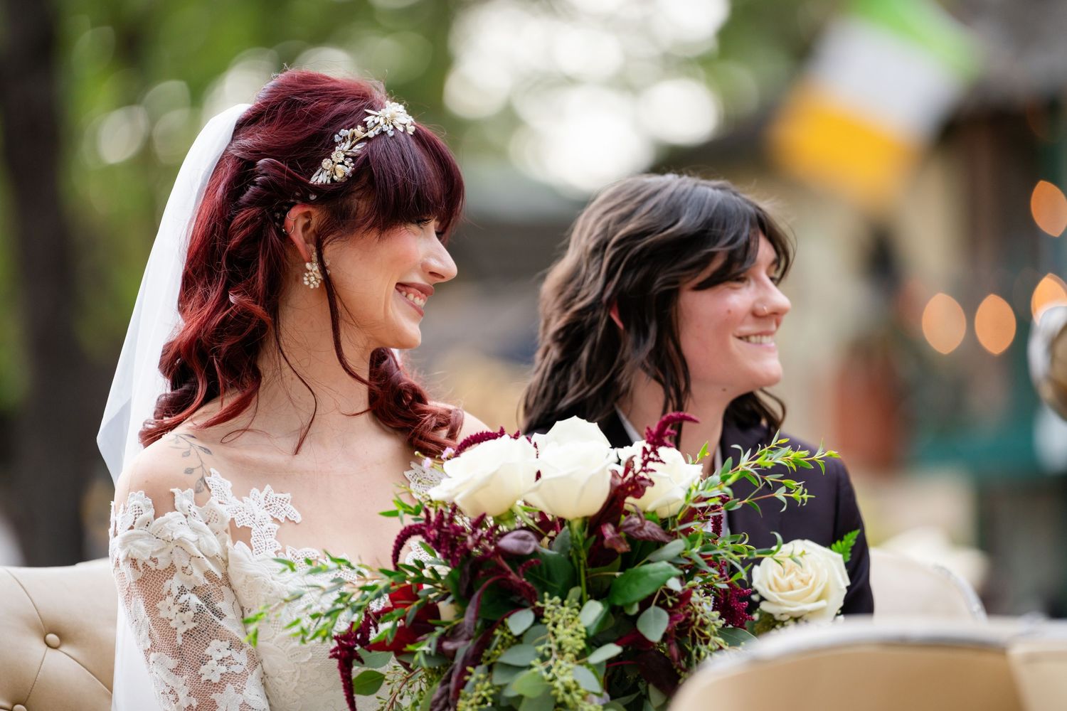 A wedding couple shares a tender moment together while holding a burgundy and white floral bouquet in an outdoor setting.