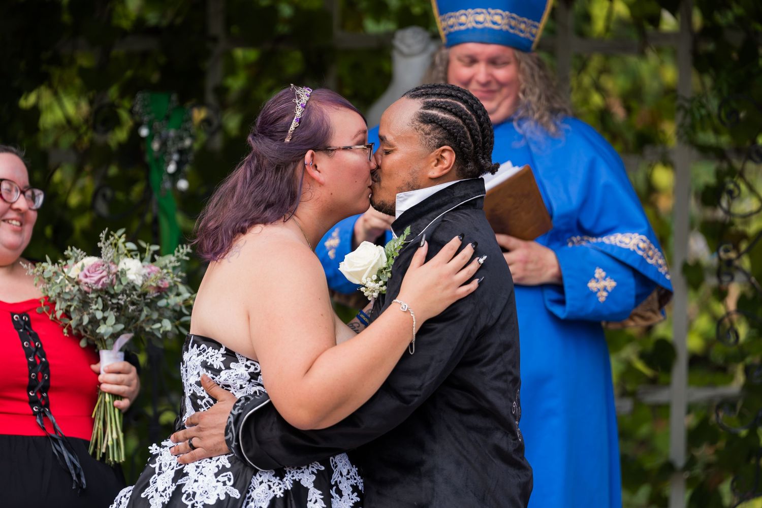 A couple in formal attire shares a tender moment during a wedding ceremony in an outdoor garden setting.