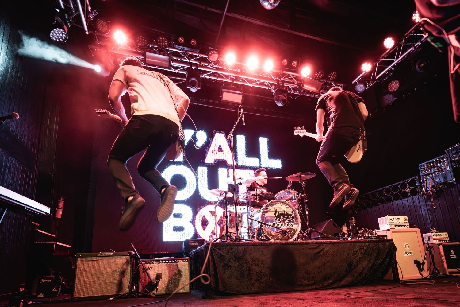 Two performers jump energetically on stage during a concert with 'Y'ALL OUT BOY' illuminated text display behind them.