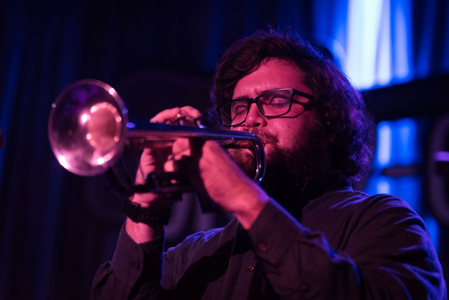 A performer plays trumpet on a dark stage illuminated by blue lighting during a jazz performance.