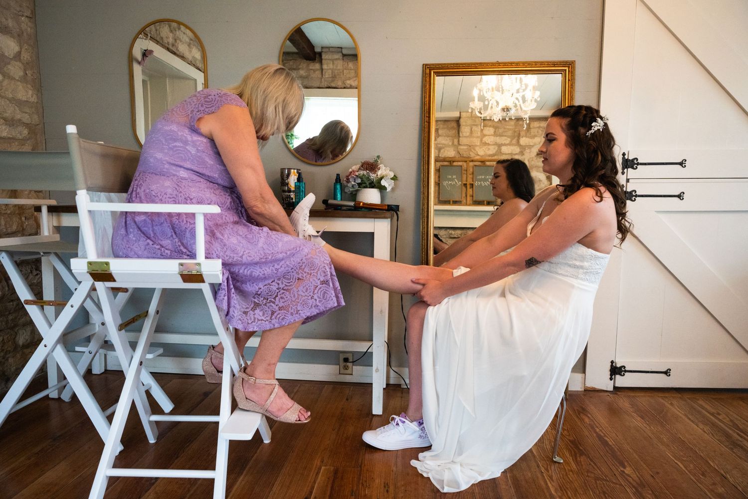 Two women share an intimate moment during wedding preparations in a rustic indoor setting.