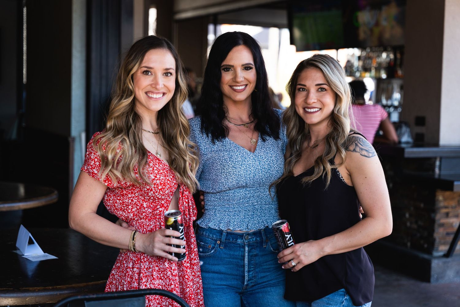 Three women smile together at a social gathering in a restaurant.