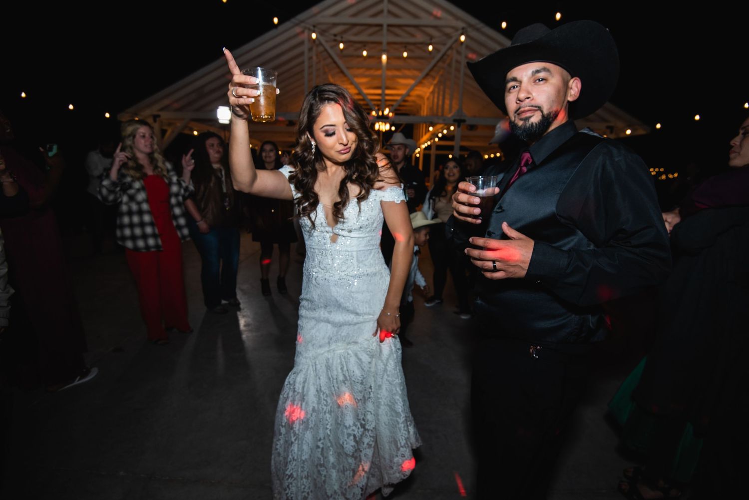 A couple raises their drinks in celebration at a festive indoor venue with string lights.