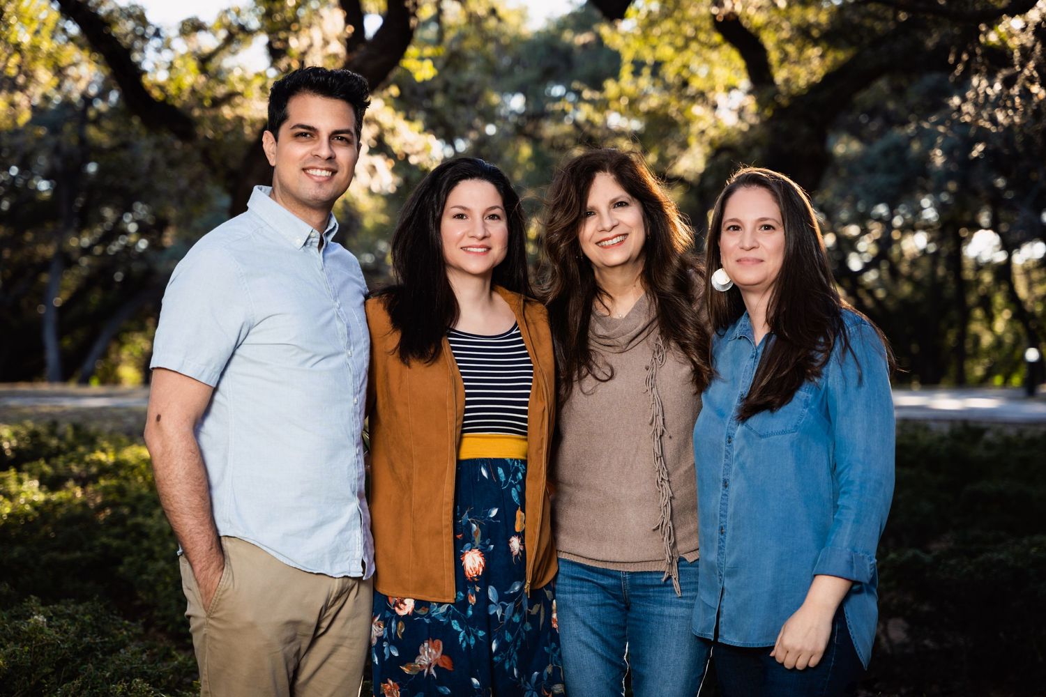 Family group portrait taken outdoors with natural lighting and foliage background.