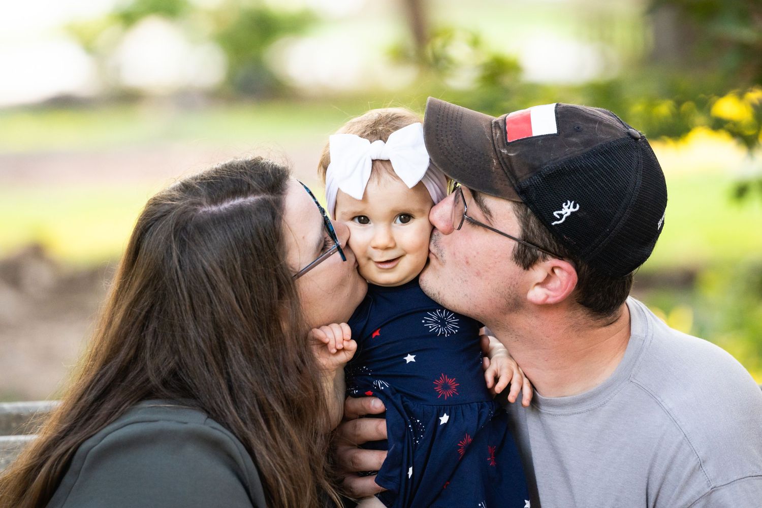 Sweet family moment captured outdoors with baby in navy dress and white bow.