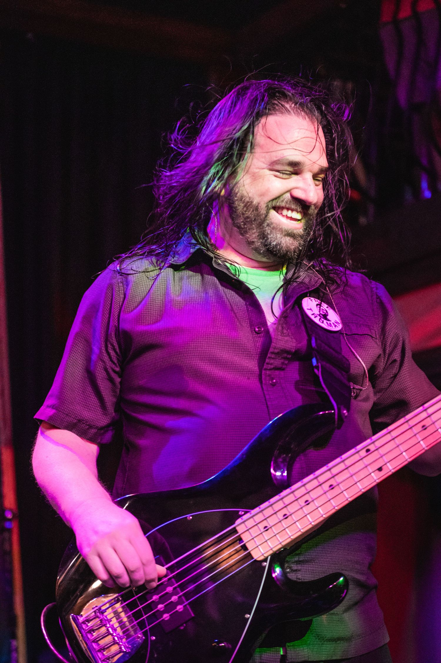 Bass guitarist performing on stage under purple lighting with an enthusiastic expression during a live concert.