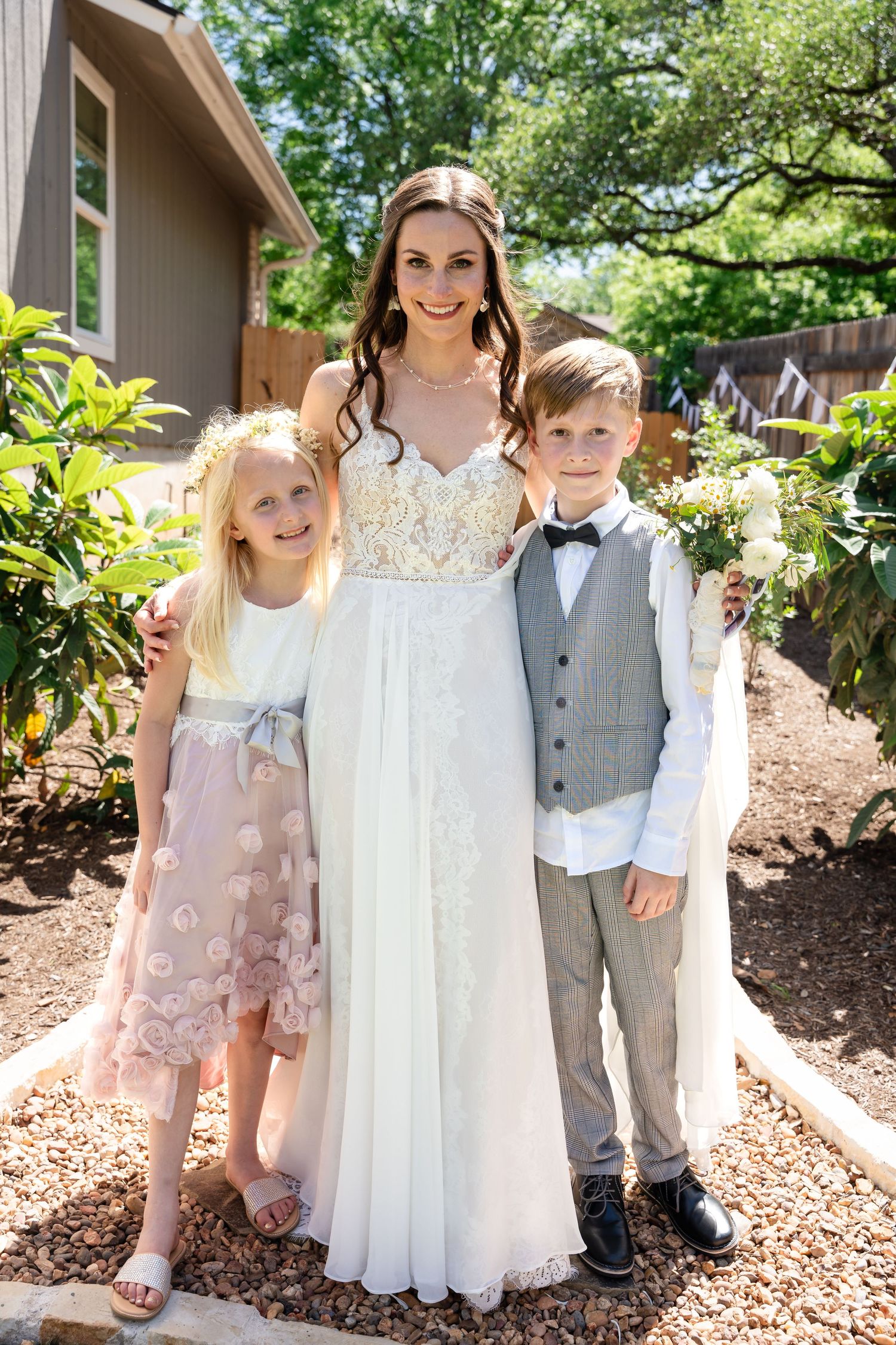 A wedding portrait with youth attendants in formal attire standing in a garden setting.