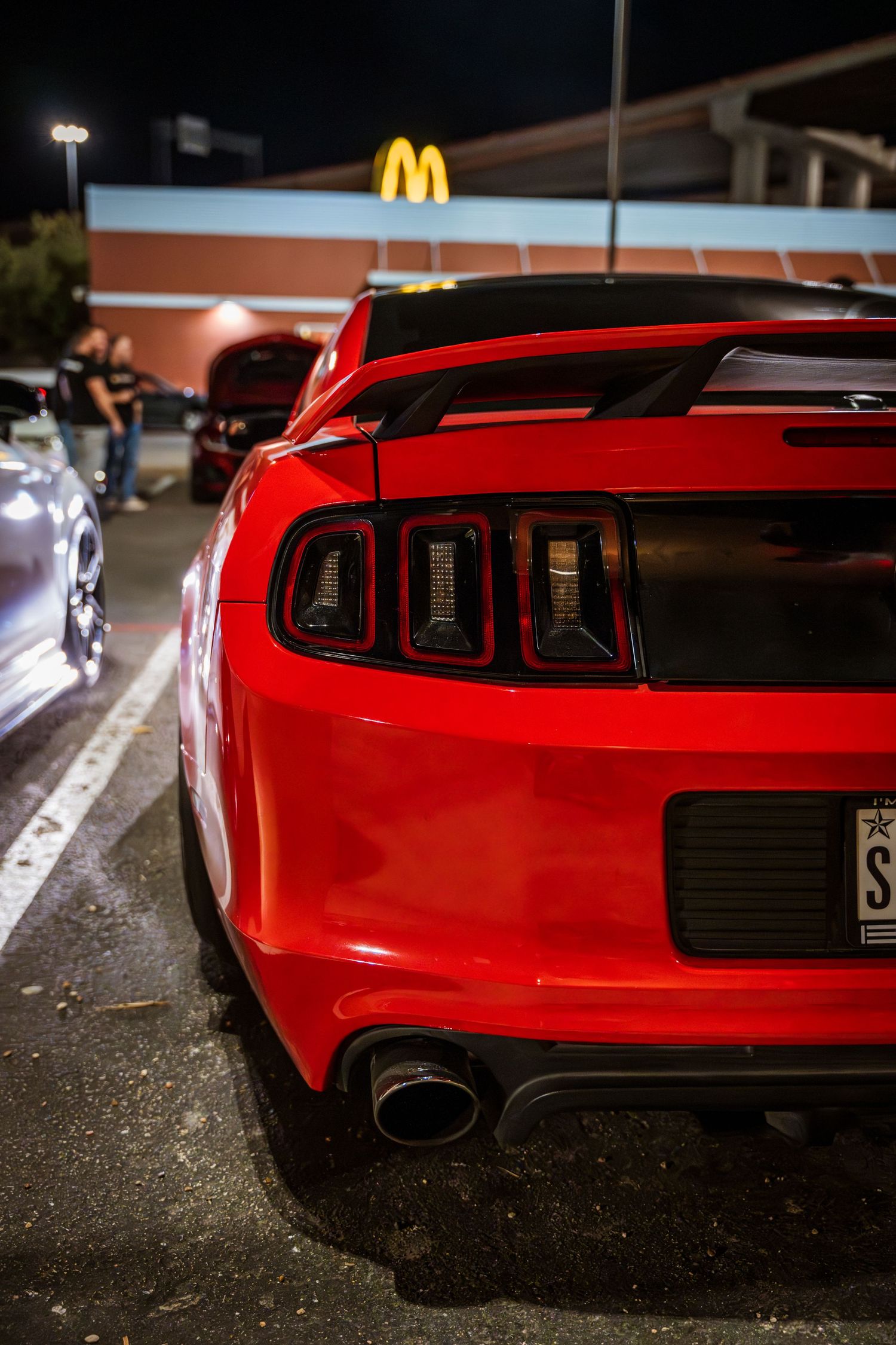 Red Mustang tail lights and exhaust with McDonald's sign in background.