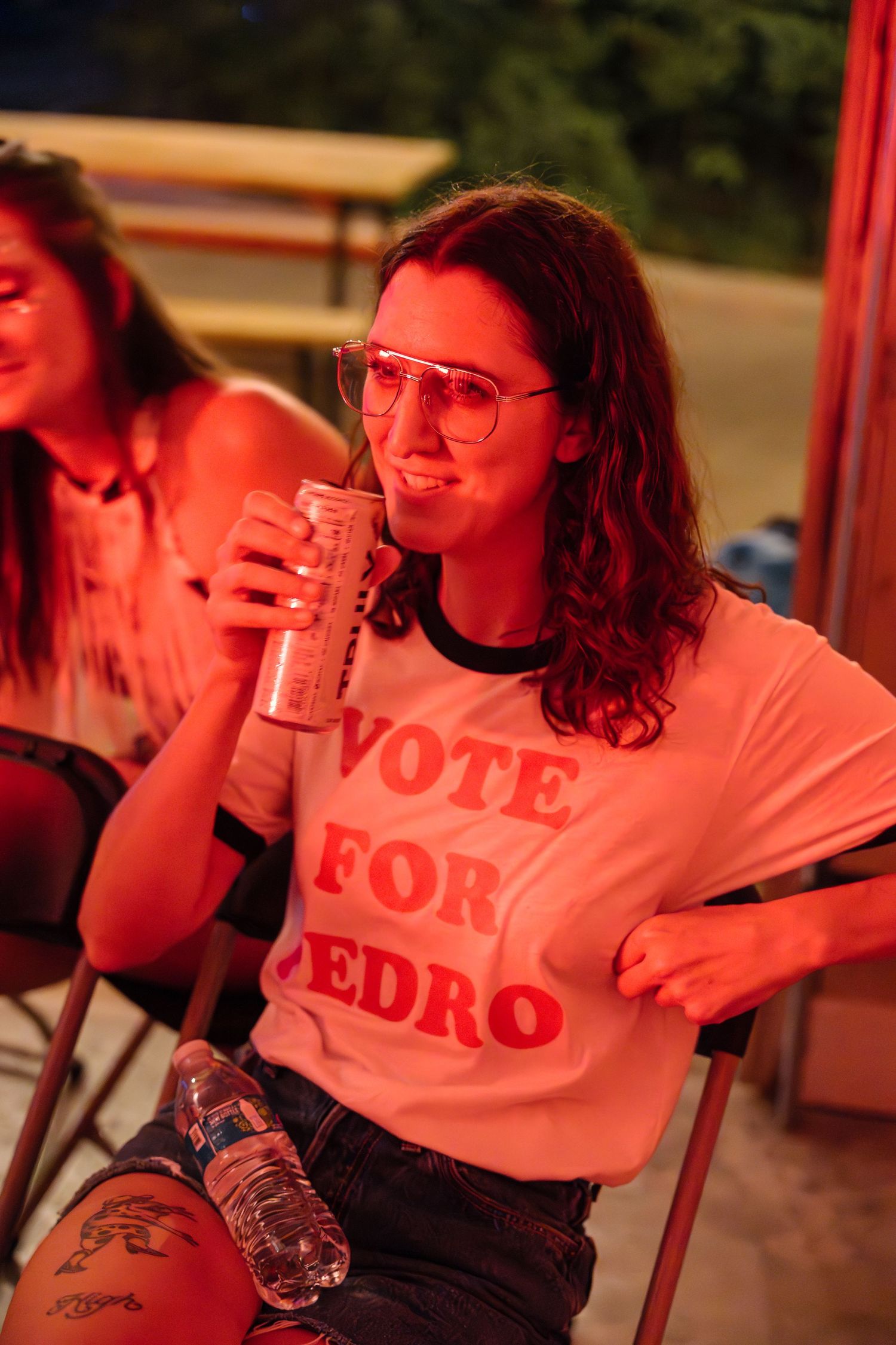 Person in a 'Vote for Pedro' t-shirt drinking from a can under warm lighting.
