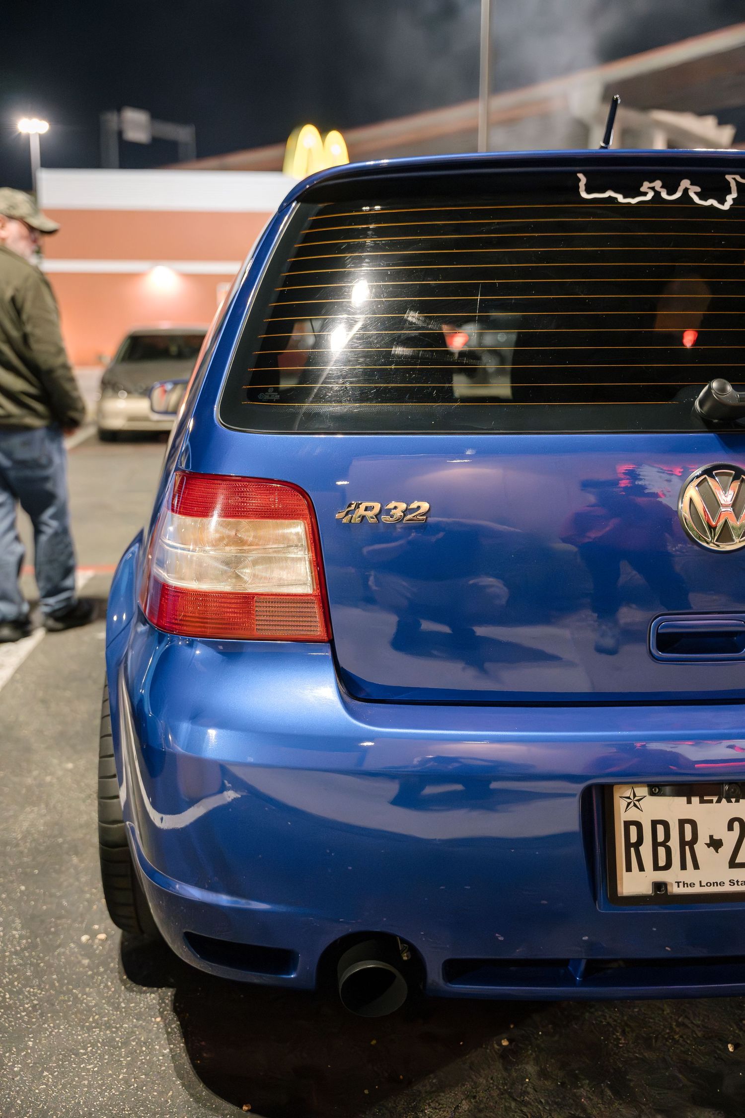 Rear view of a blue Volkswagen R32 at night in a parking lot.