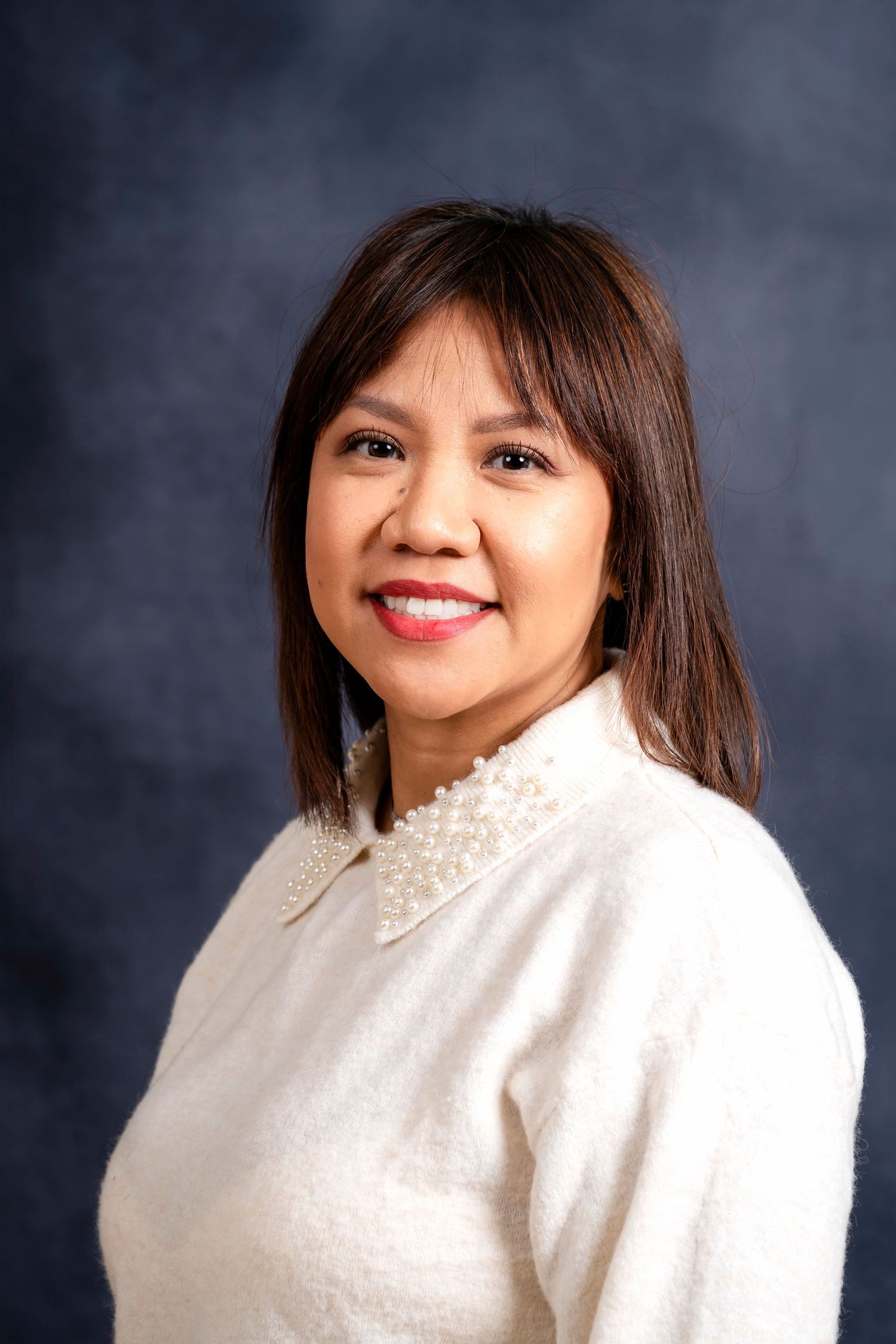 Professional portrait of woman in white pearl-collar sweater against gray backdrop.
