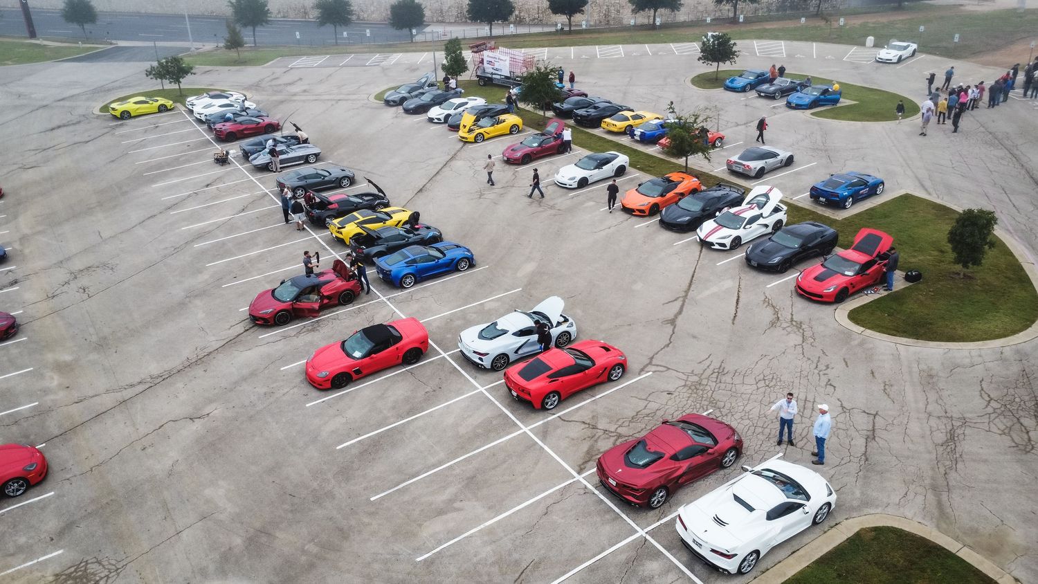 Birds-eye view of diverse sports cars lined up for a car show in a large parking area.