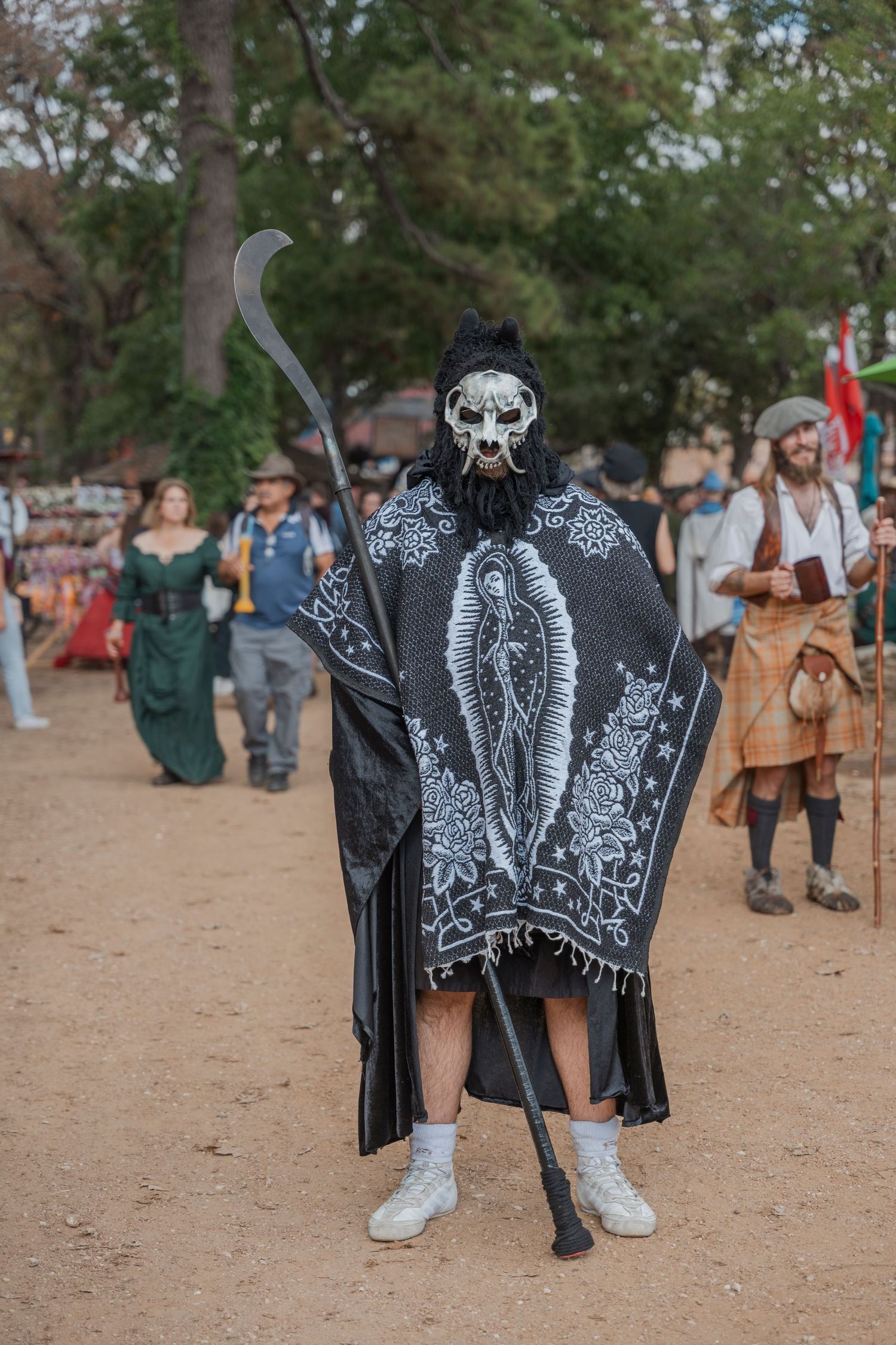 Person in dark costume wearing skull mask and holding staff at Renaissance festival.