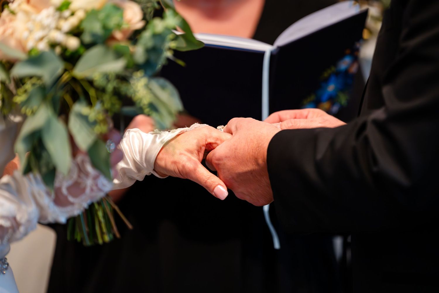 Close-up of hands exchanging rings during a wedding ceremony with an officiant holding a book.