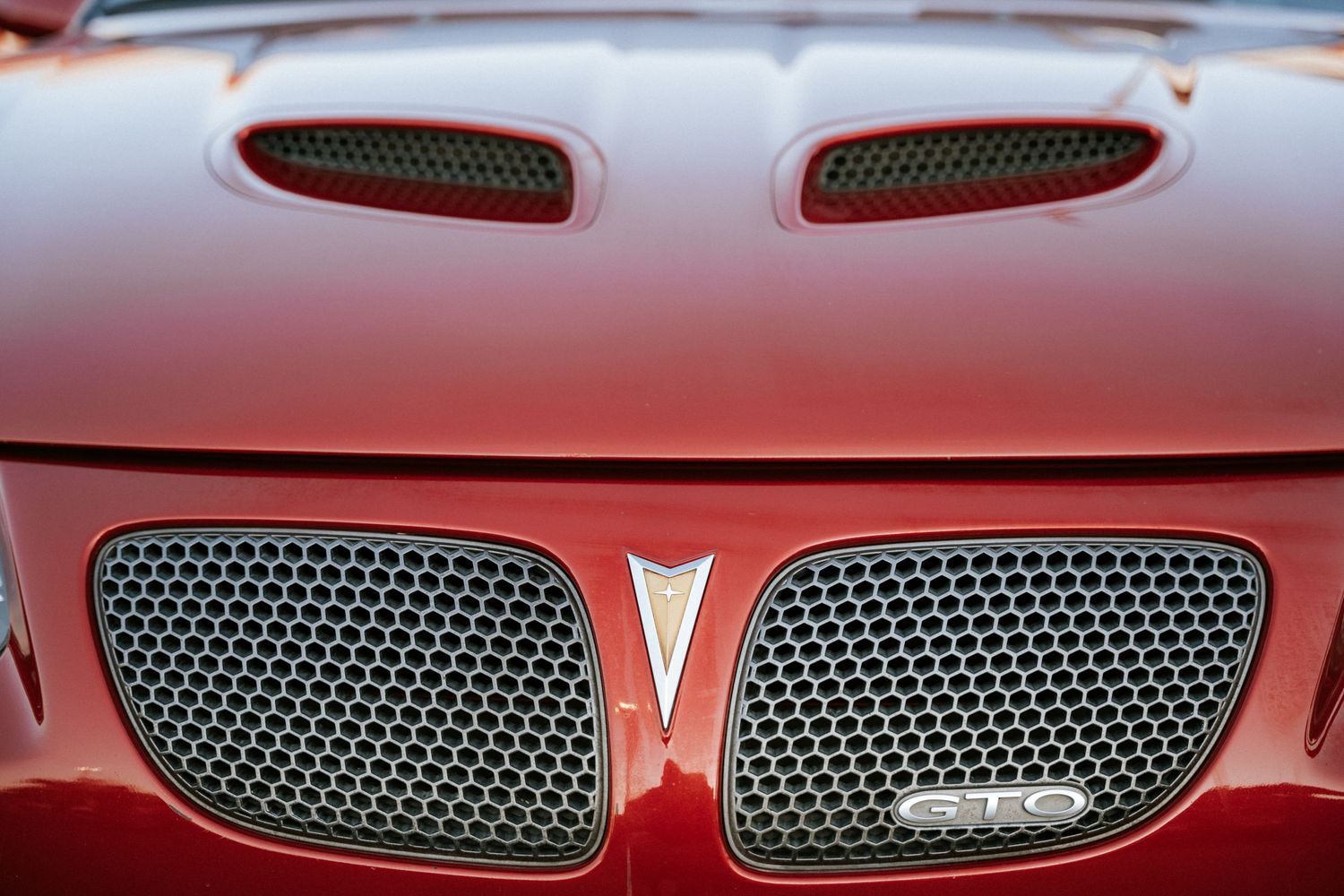 Close-up detail of a red Pontiac's hood vents and mesh grille.