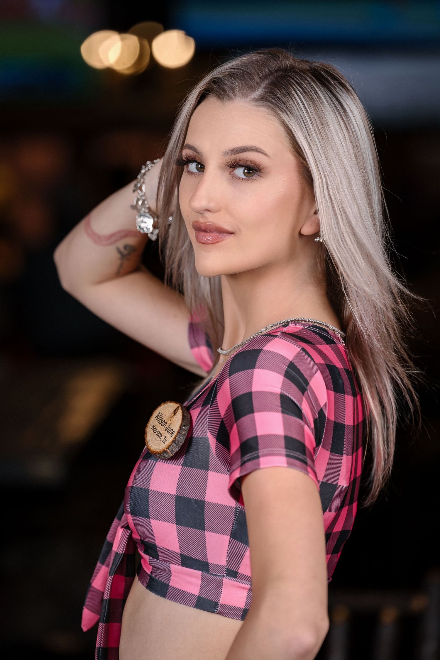 Portrait of woman in pink plaid crop top with platinum blonde hair against evening setting.