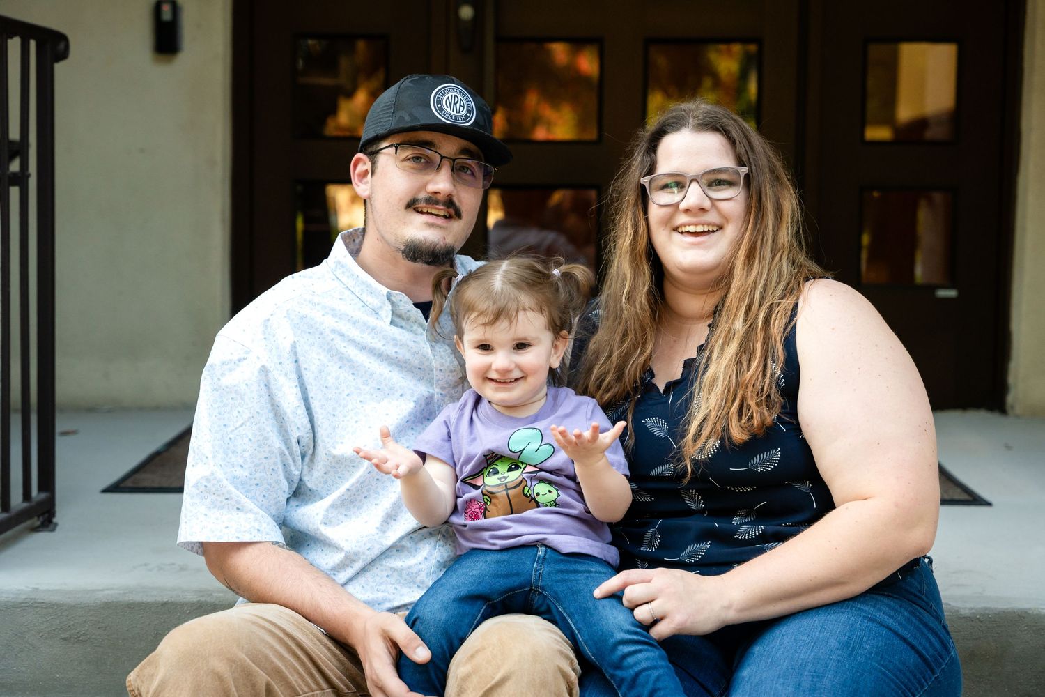 Family sitting together on concrete steps outside a building.