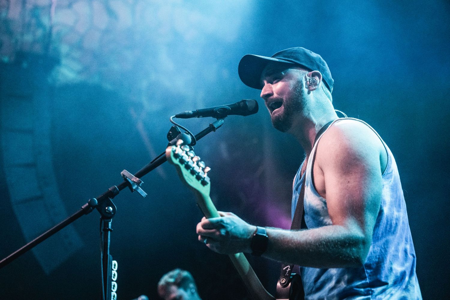 Musician sings and plays guitar under blue stage lighting during concert performance.