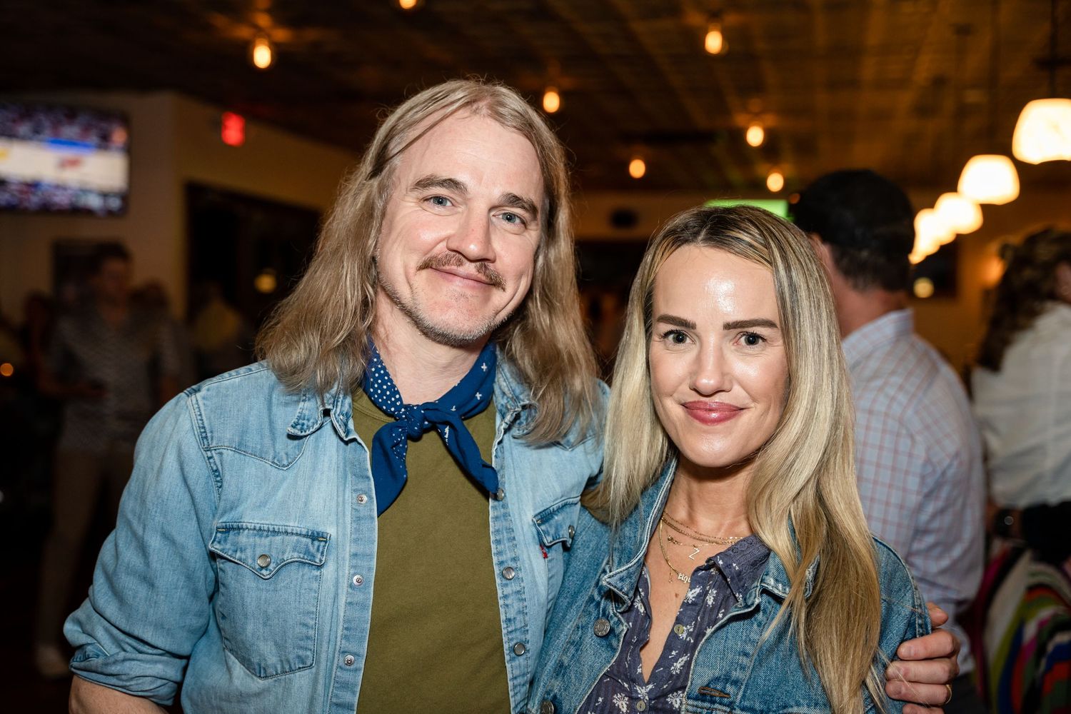 Two companions in casual denim and earth tones pose together at an evening social event.