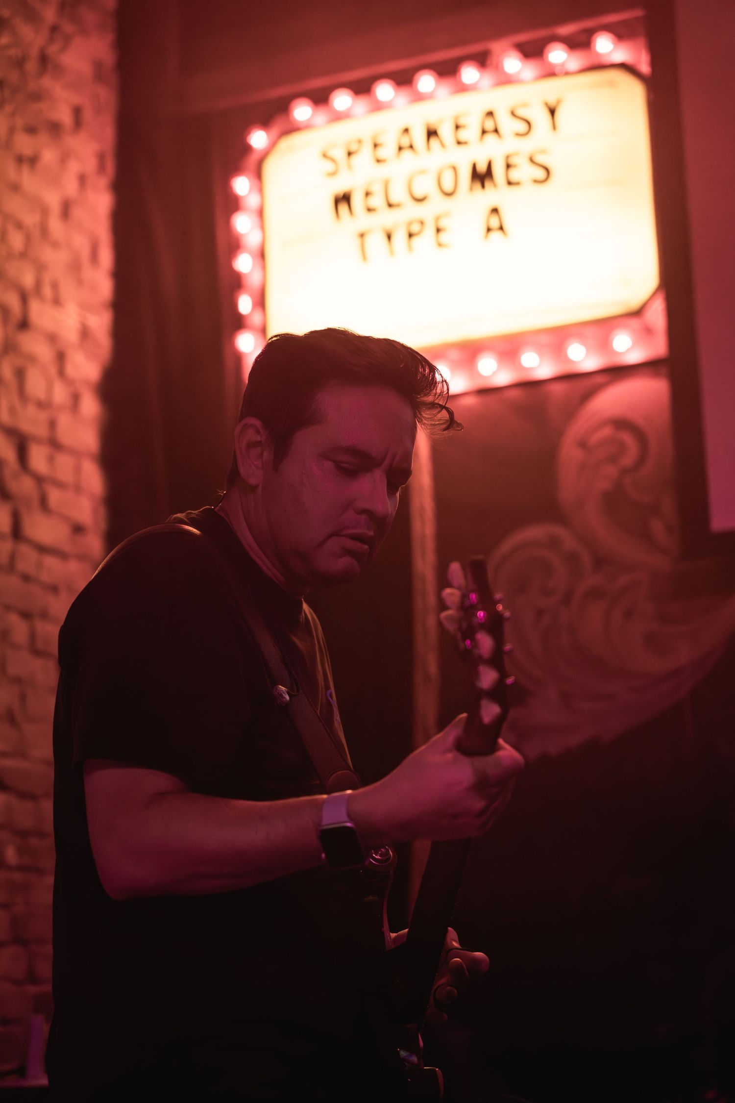 A musician performs under red lighting with a vintage-style marquee sign in the background.