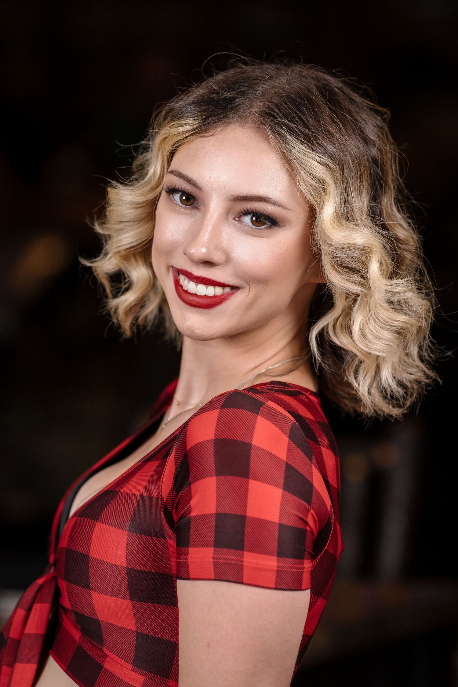 Woman wearing red buffalo plaid top with curled blonde hair and red lipstick.