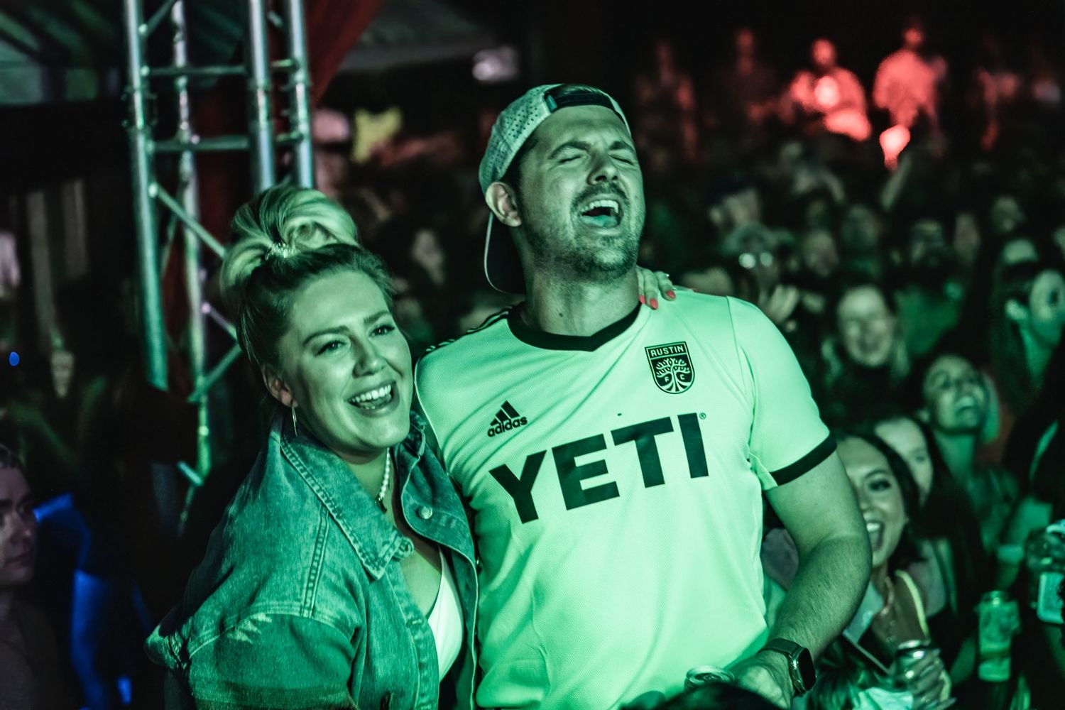 Concert attendees enjoy music under green stage lighting.