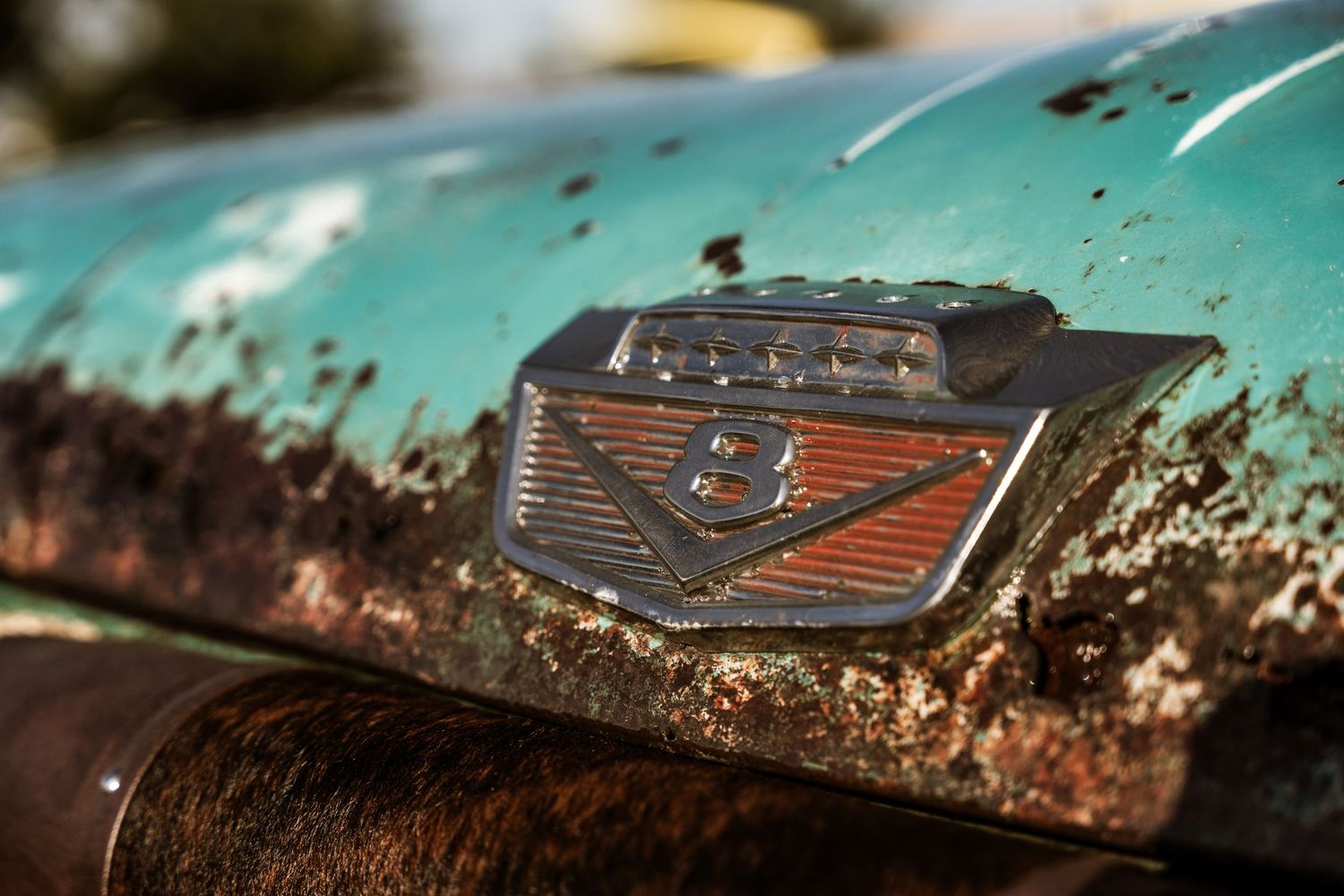 Weathered Ford emblem badge on a rusty turquoise vehicle hood.