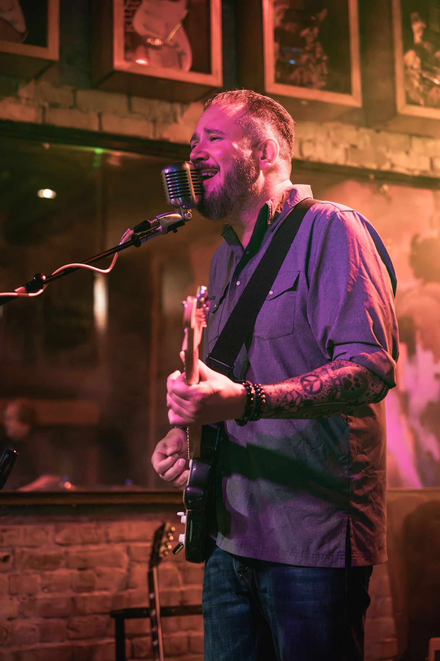 Singer performing with guitar at intimate venue with vintage microphone and brick walls.