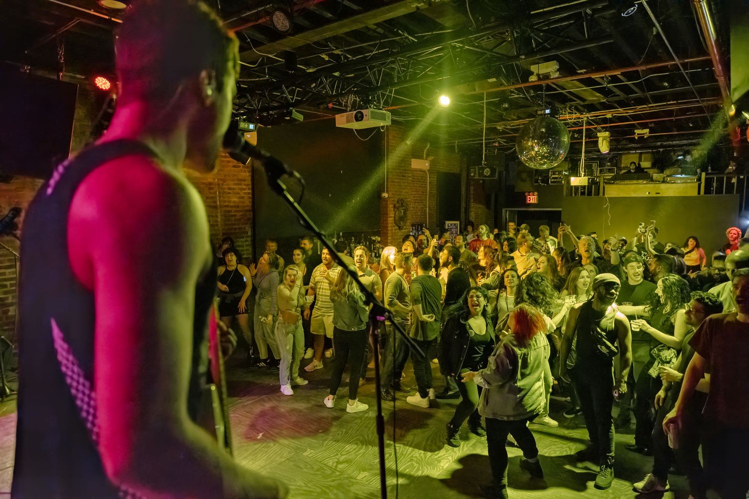 Concert crowd watching performer on stage under vibrant pink and green lighting.