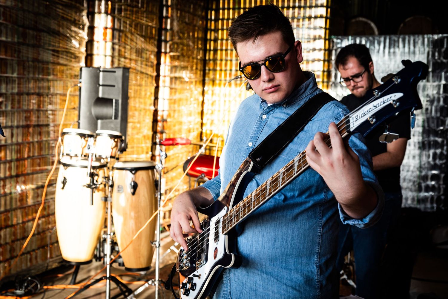 Bass guitarist performs in front of brick wall with dramatic lighting.