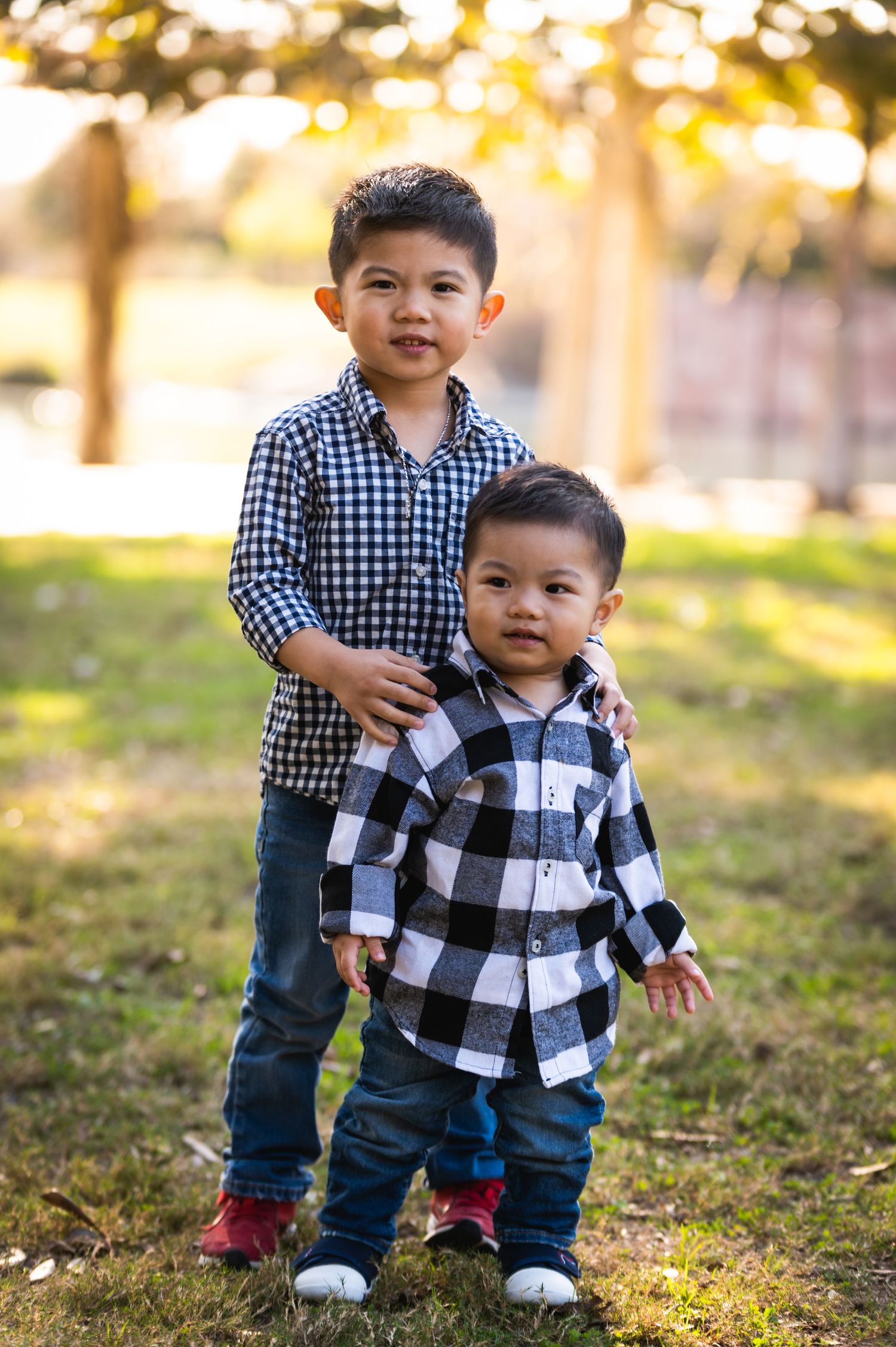 Two children in plaid shirts stand together outdoors during a photo session.