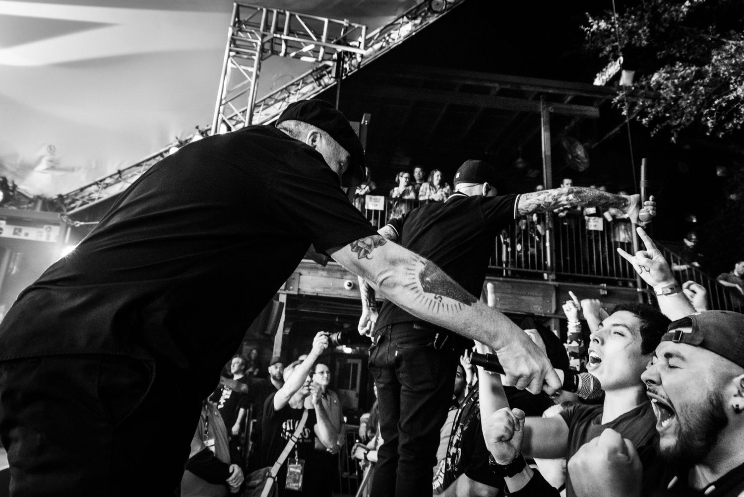 Concert performer leans into crowd during high-energy performance as fans reach up in excitement.