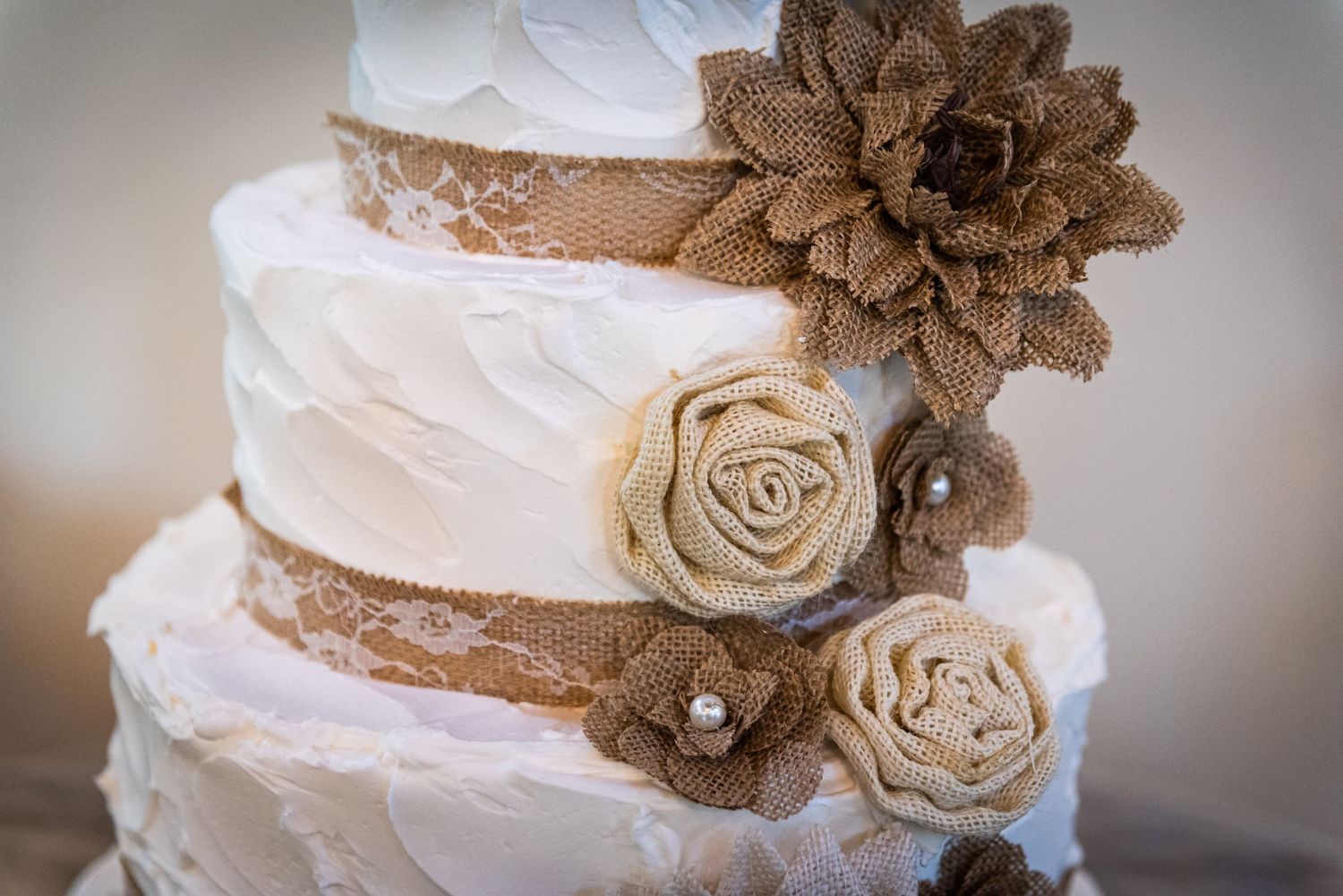 Three-tiered white wedding cake decorated with burlap flowers and ribbons.