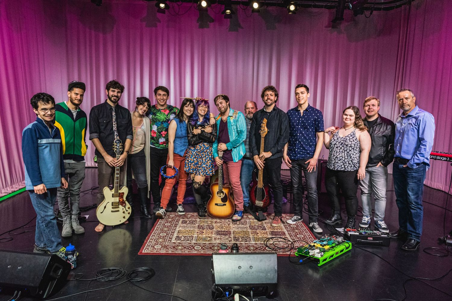 Large ensemble of musicians gather for group photo with instruments on stage.