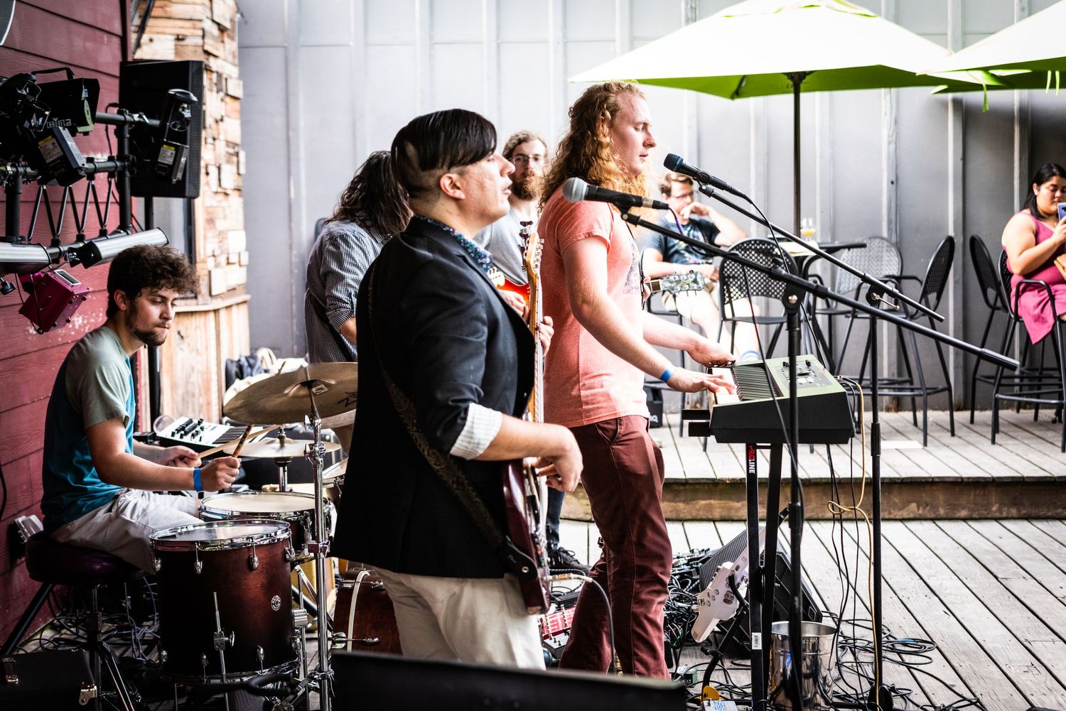 Live band performs on wooden deck stage with microphones and instruments setup.
