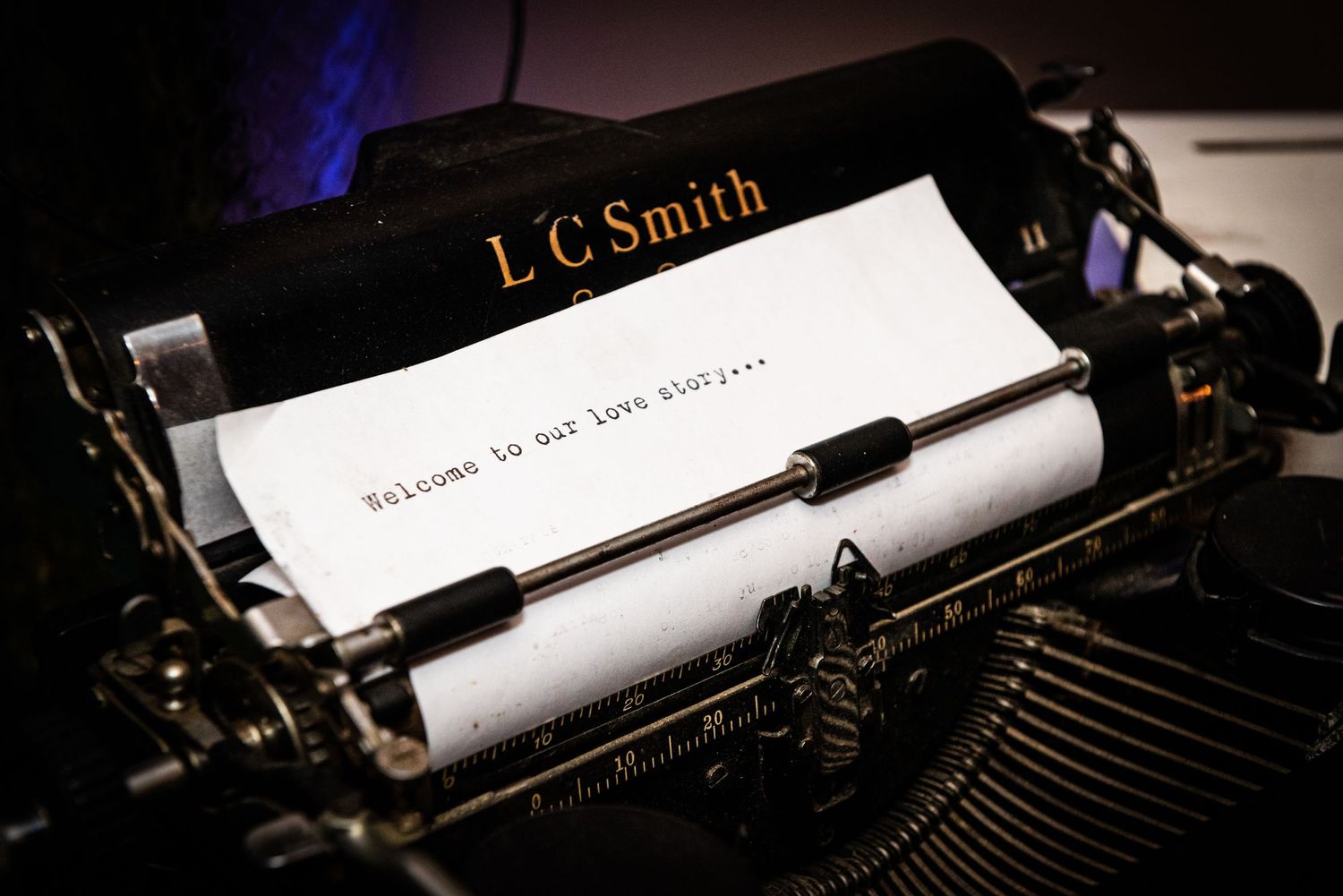A vintage typewriter with 'LC Smith' branding displays wedding story text on white paper.