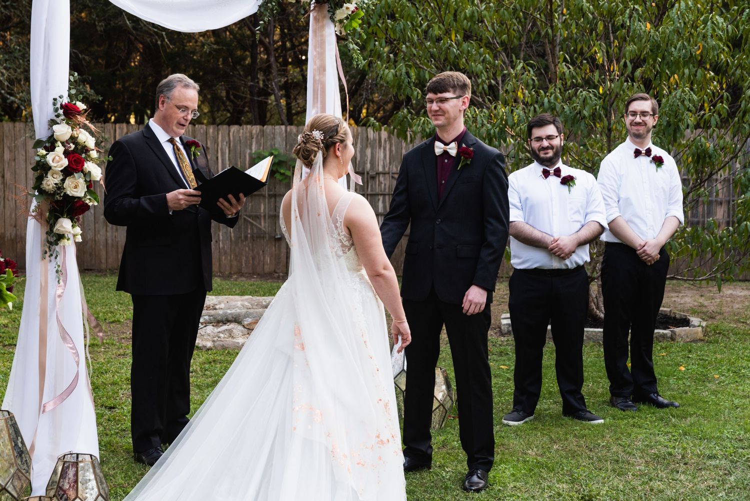 An outdoor wedding ceremony scene with attendants in formal attire and white decorative elements.