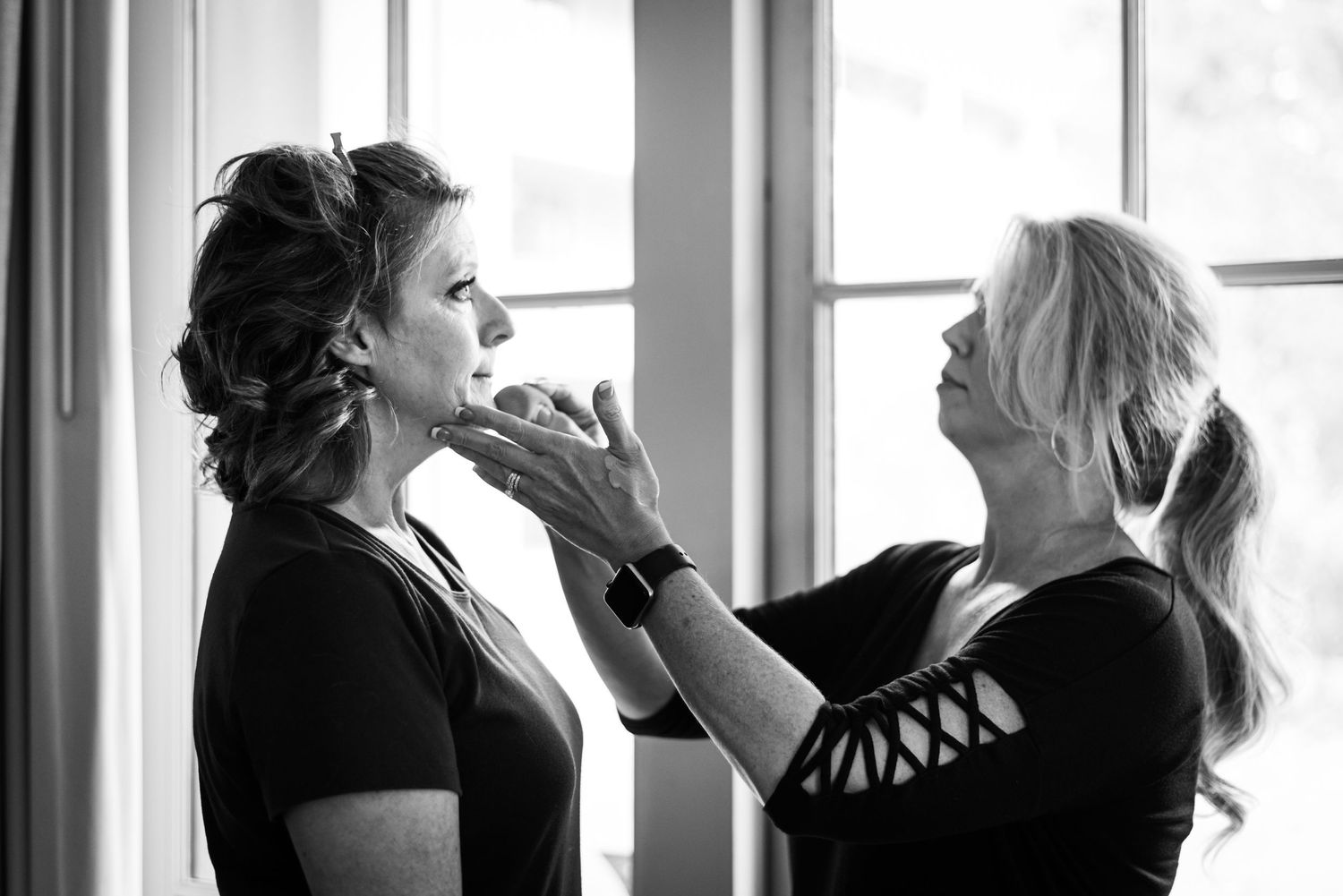 Professional makeup artist applying cosmetics in natural window light.