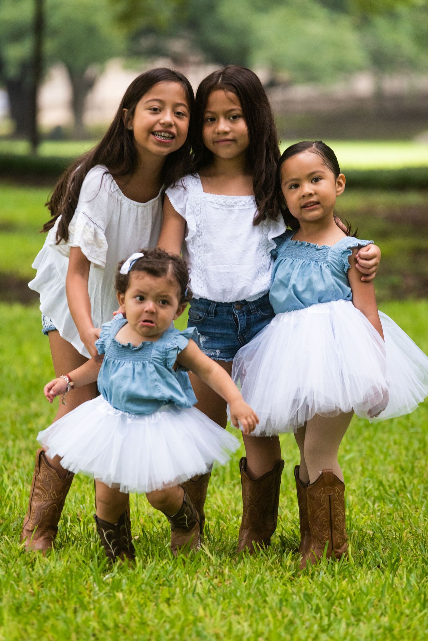 Four siblings pose together outdoors wearing coordinated outfits with tutus and cowboy boots.