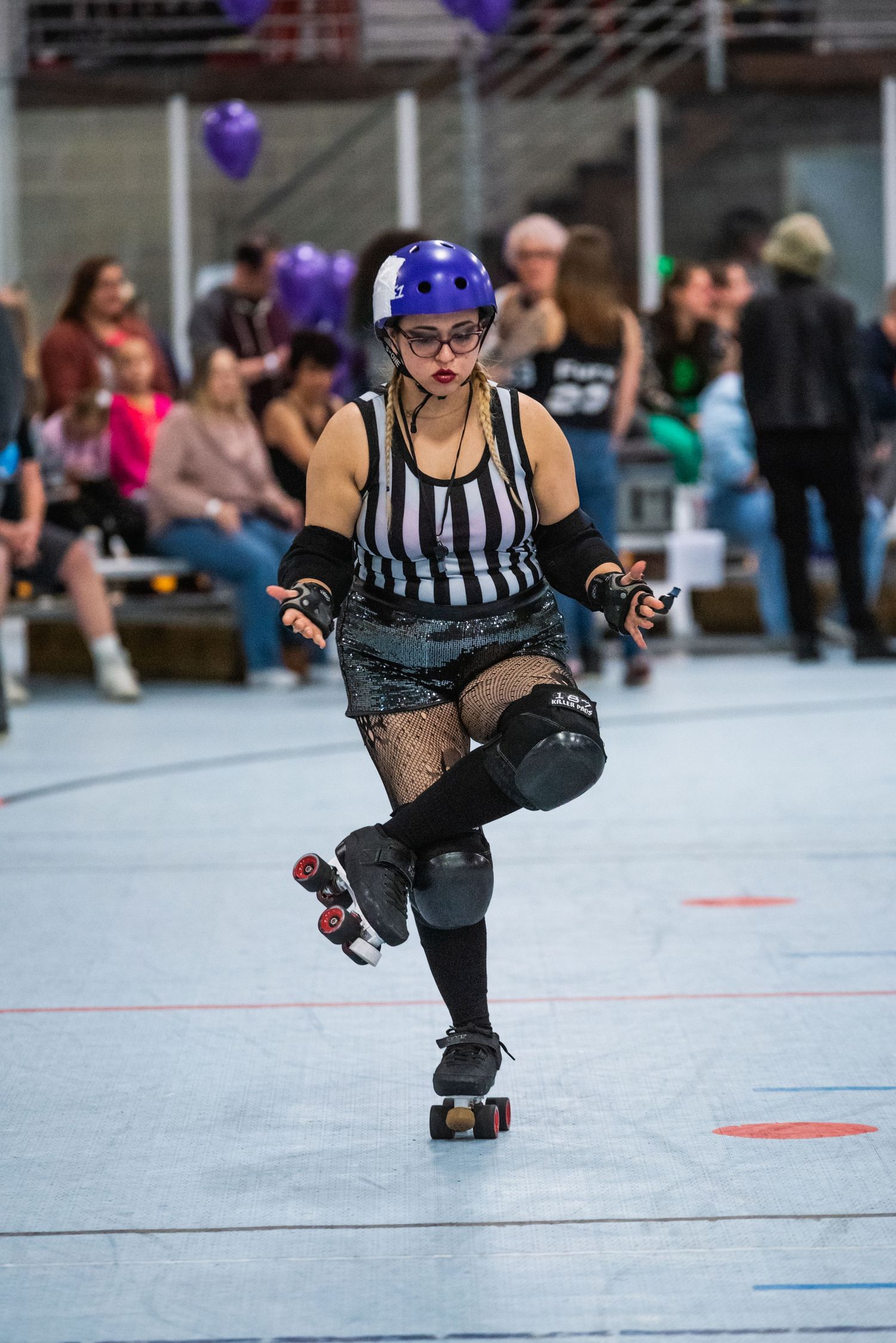 Referee in striped uniform performs on roller skates during derby match.
