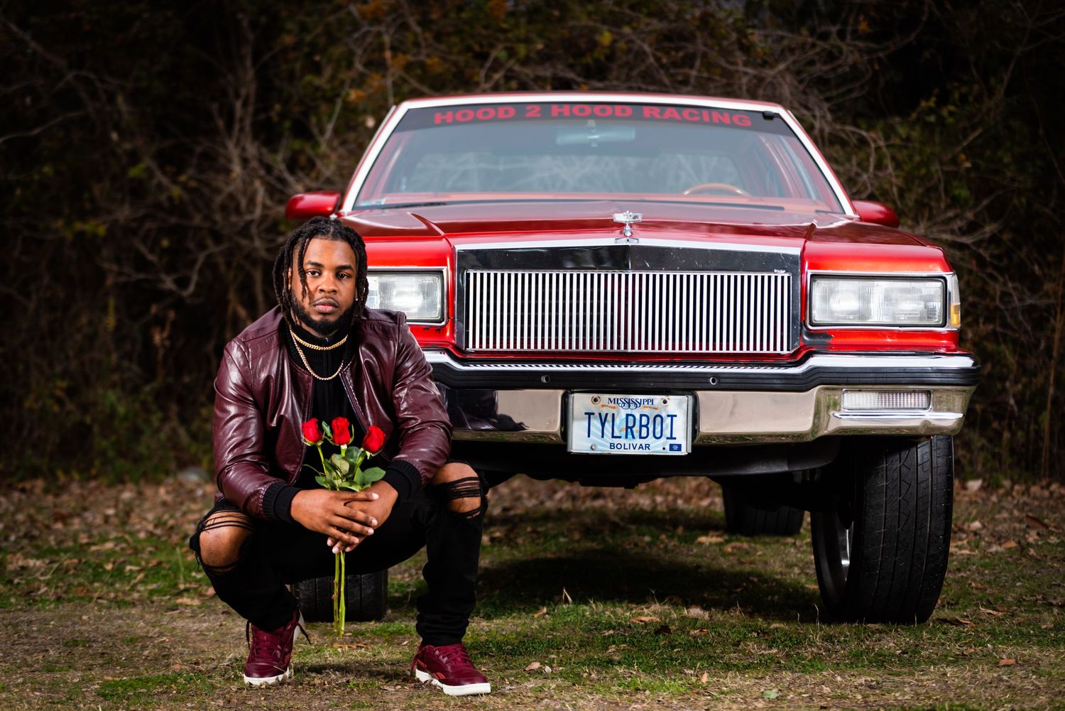 Low angle shot of person crouching in front of classic red car with chrome grille.