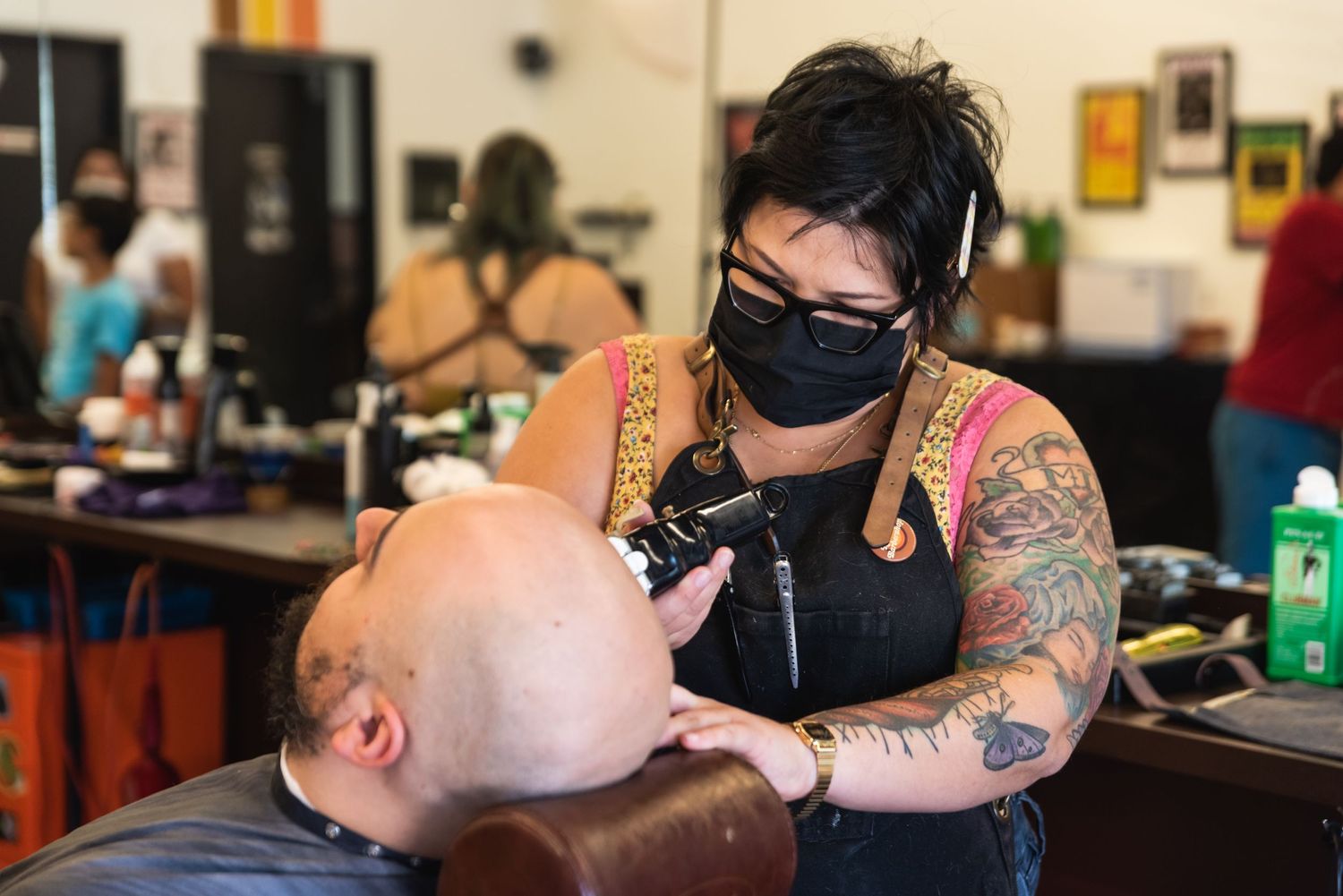 Tattooed barber in mask and apron giving a client a haircut in a modern salon.