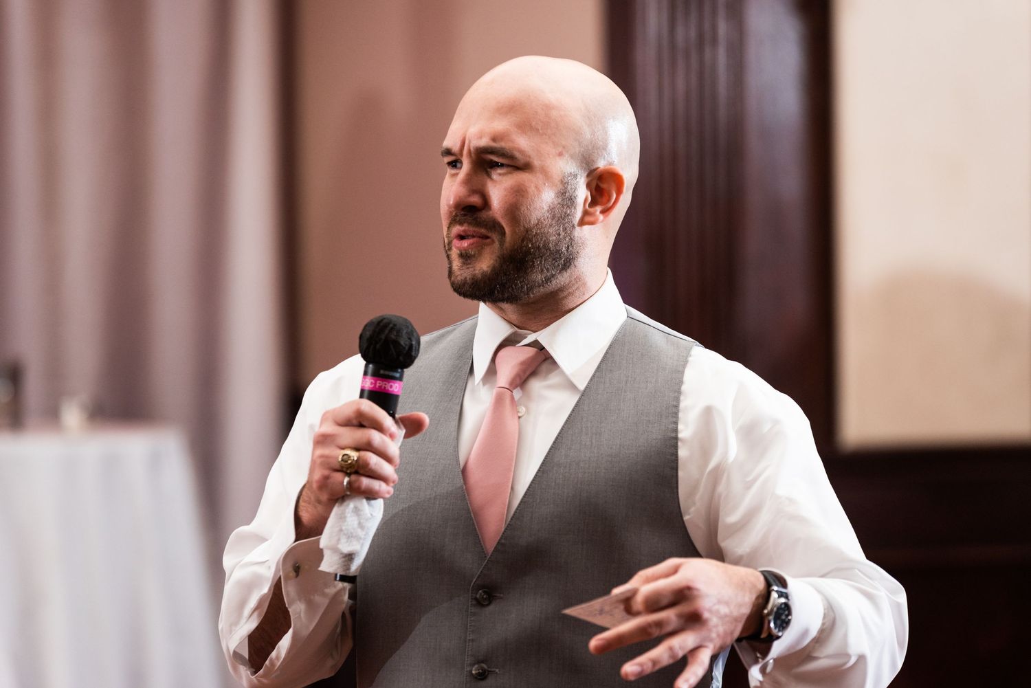 Wedding speaker delivering toast in grey vest and pink tie.