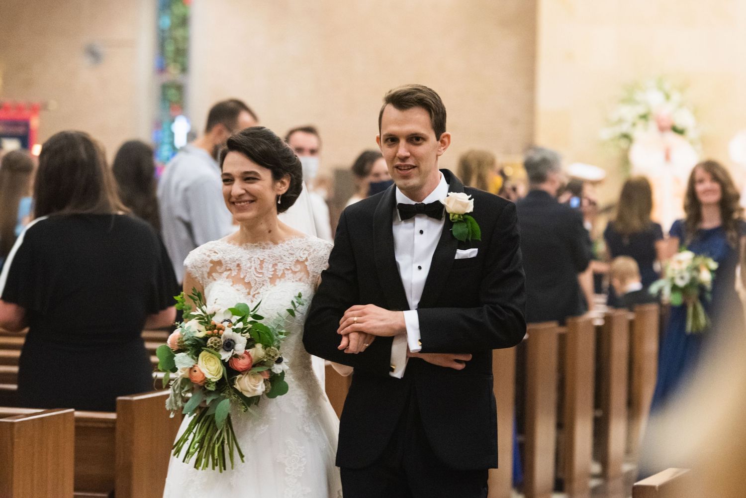 Newlywed couple walking down church aisle with bride holding floral bouquet.