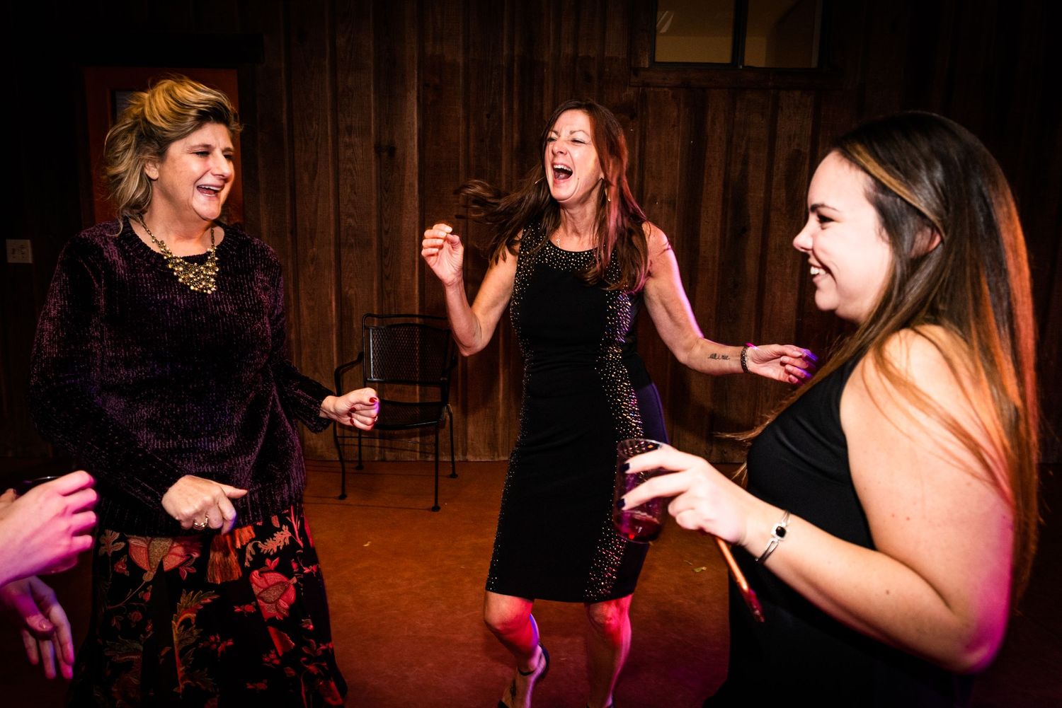 Three people dancing enthusiastically at indoor wedding reception.