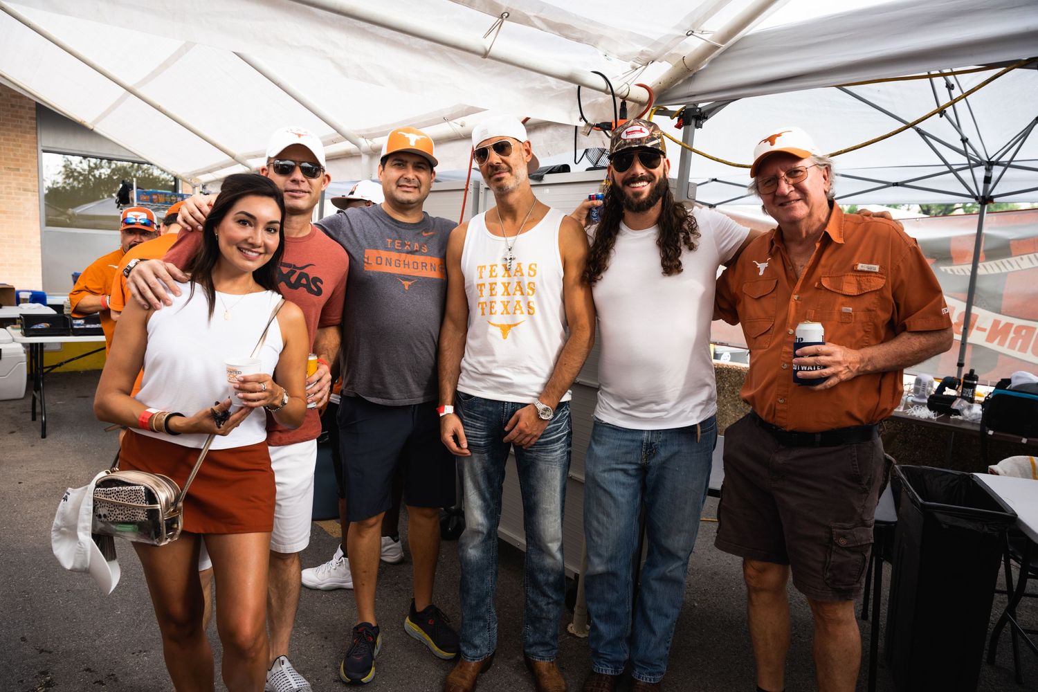 Group of festival attendees in casual wear pose together under white tent.