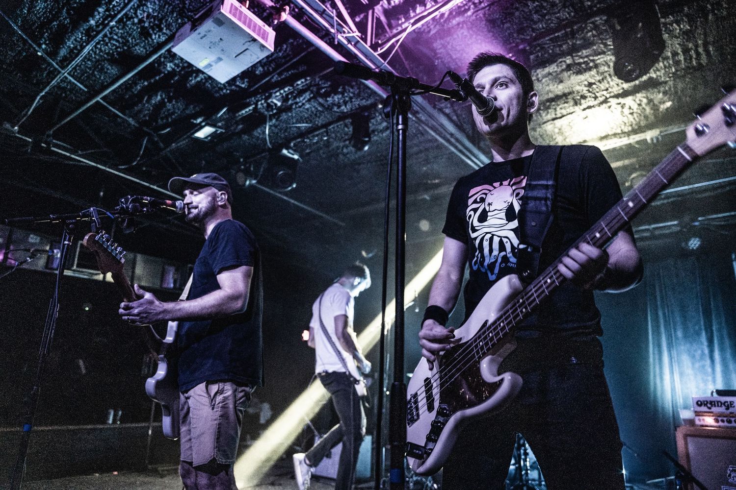 Band members perform intense rock music on dimly lit stage with dramatic lighting effects.