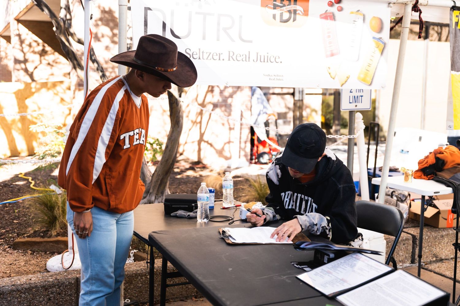 A person in orange shirt talking to someone at event merchandise table.