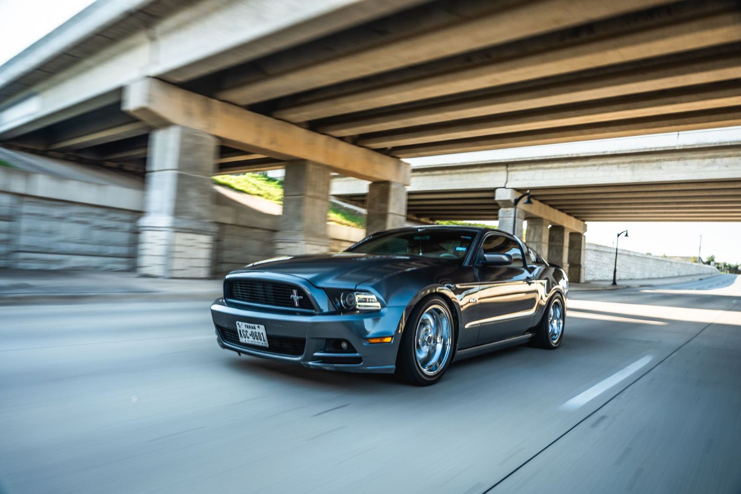 Blue Ford Mustang driving under a concrete overpass with motion blur effect.